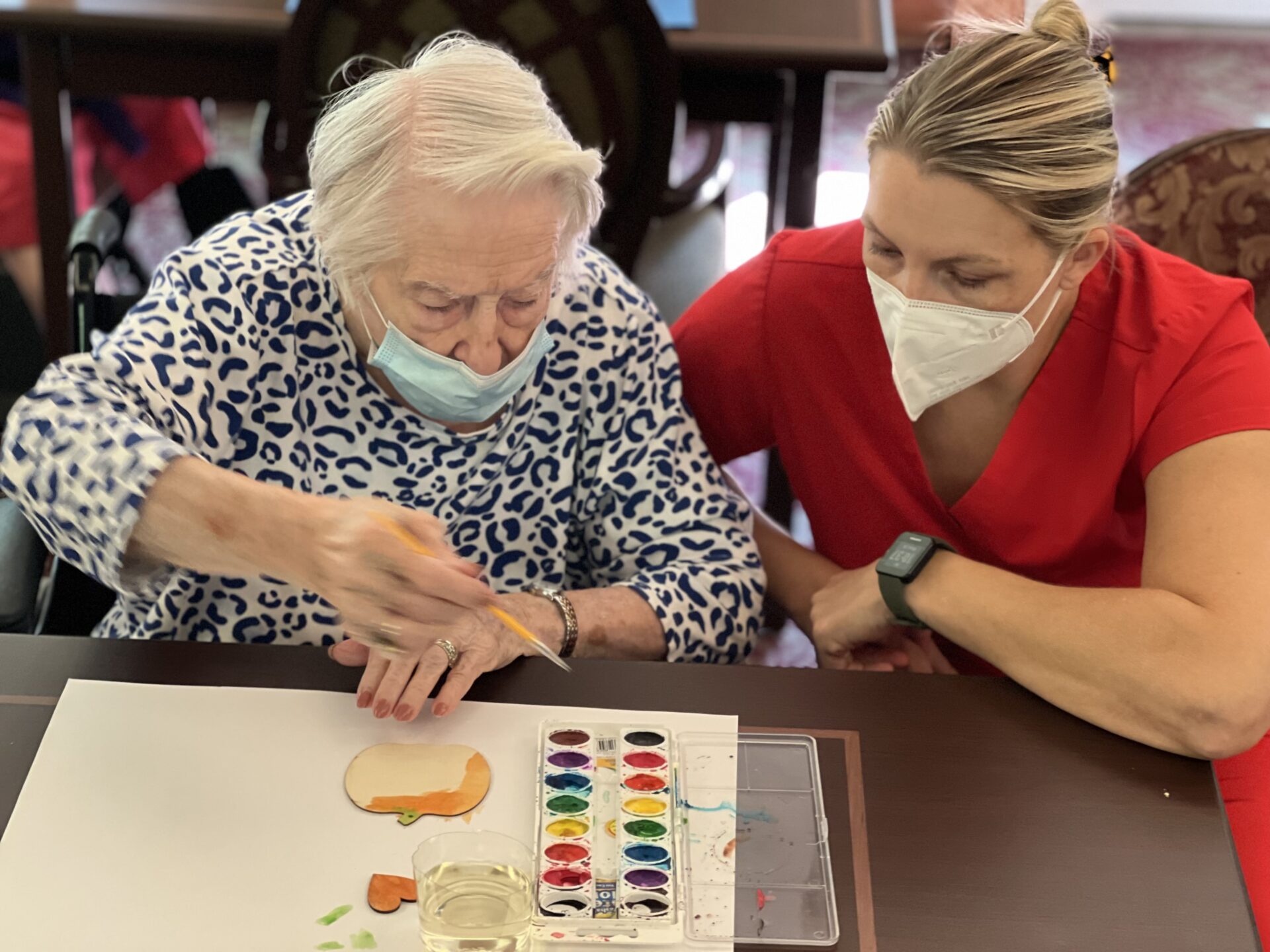 rehab staff crouching beside a patient painting a craft